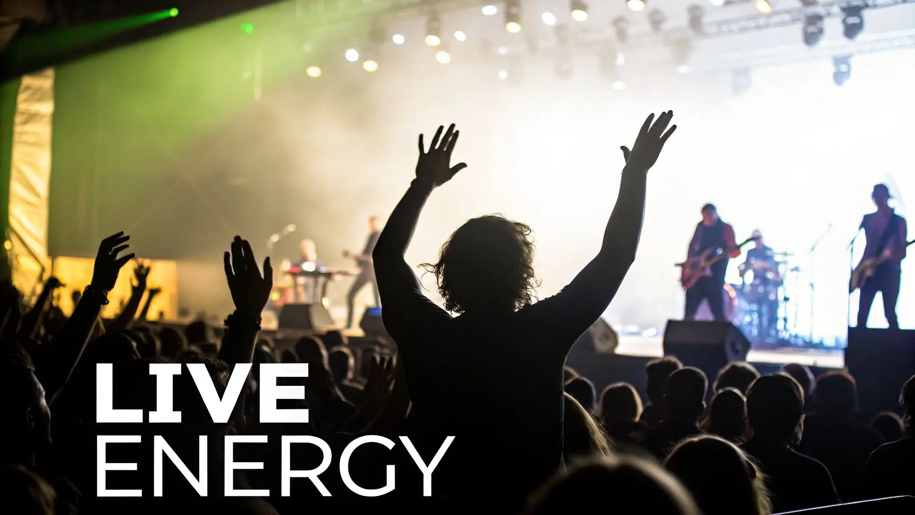 Silhouetted crowd with raised hands at a vibrant live music concert with a band on stage.