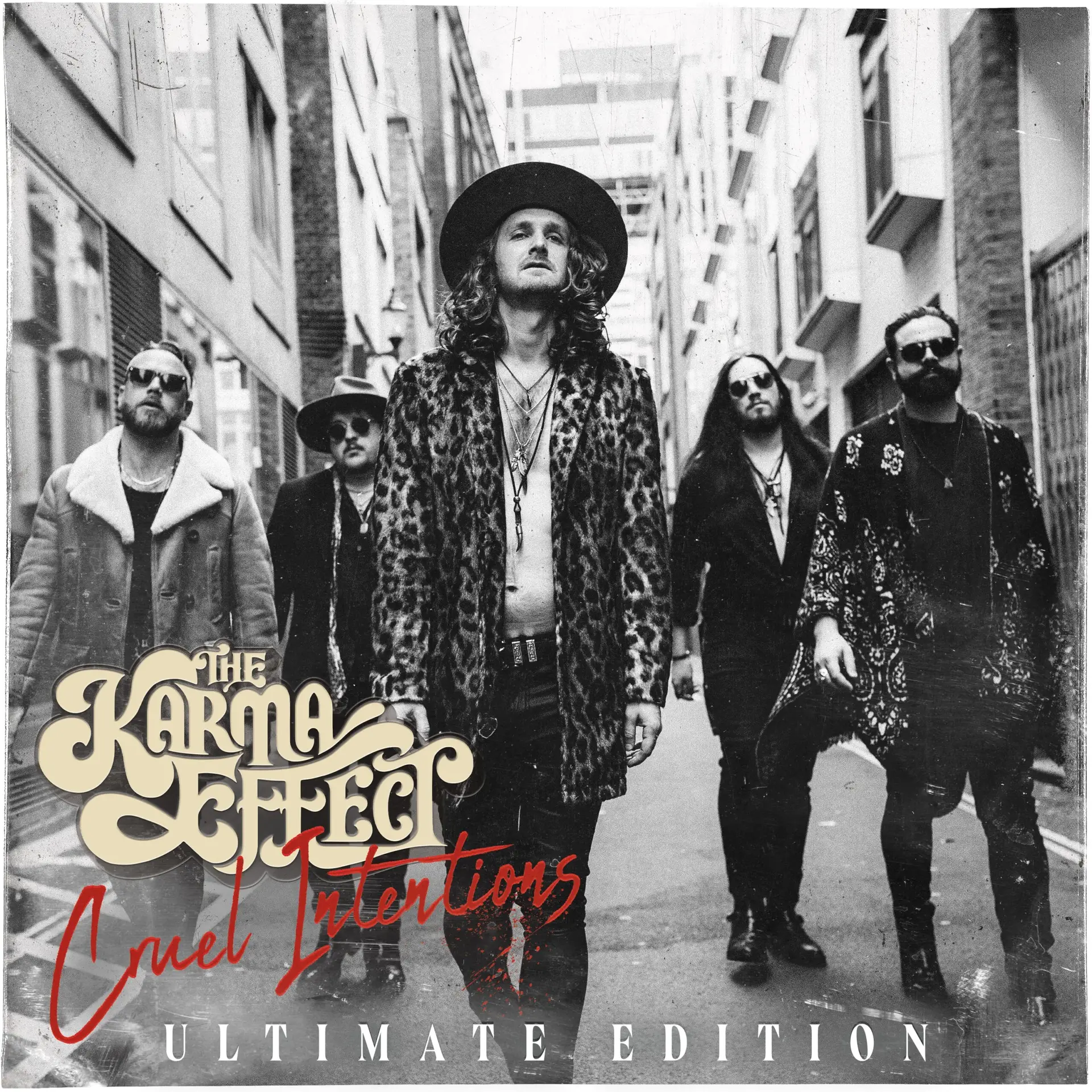 Black-and-white promotional photo of a rock band walking down a narrow city street, led by a man in a leopard print coat and wide-brimmed hat, with overlaid bold typography and 'Ultimate Edition' text at the bottom.